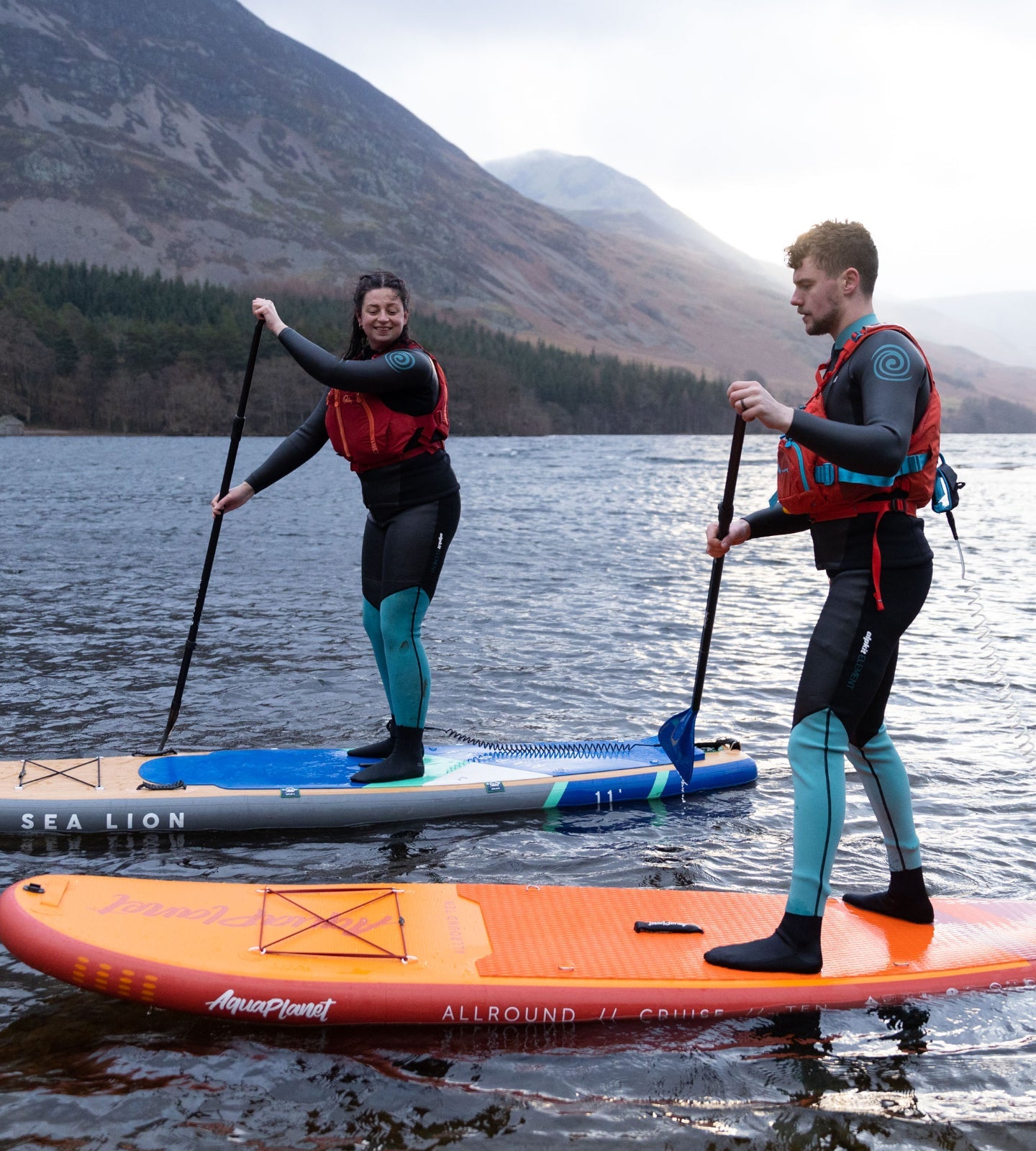 Paddle boarders in wetsuits paddle boarding in the Lake District