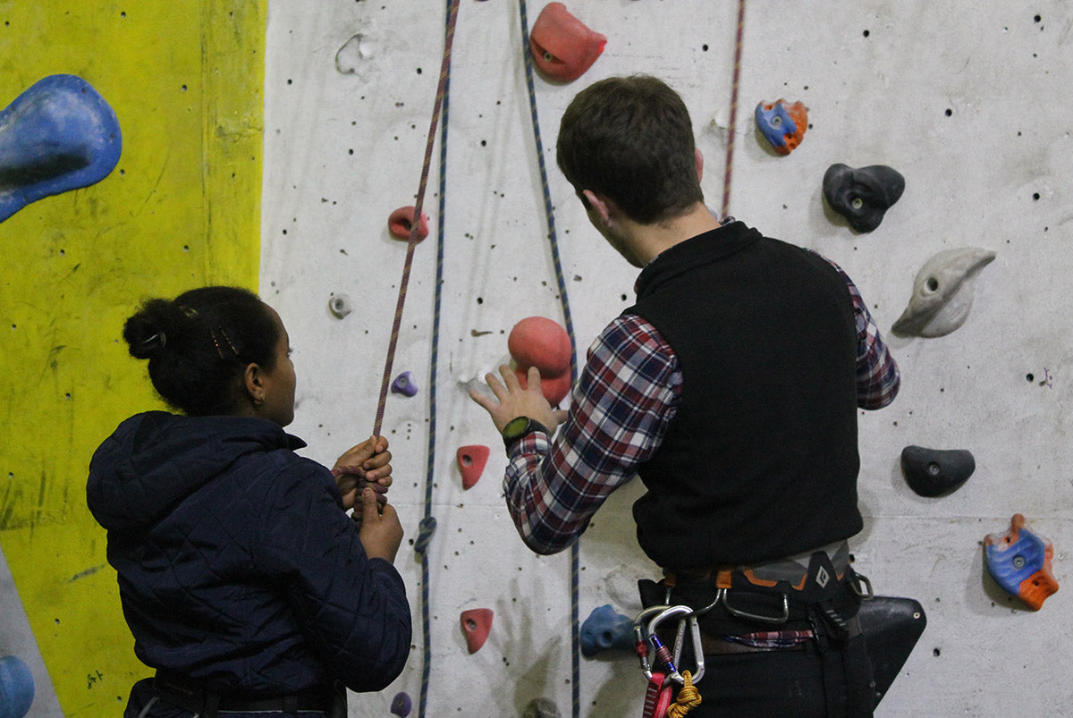 A young person climbing on an indoor wall, reaching for the next hold
