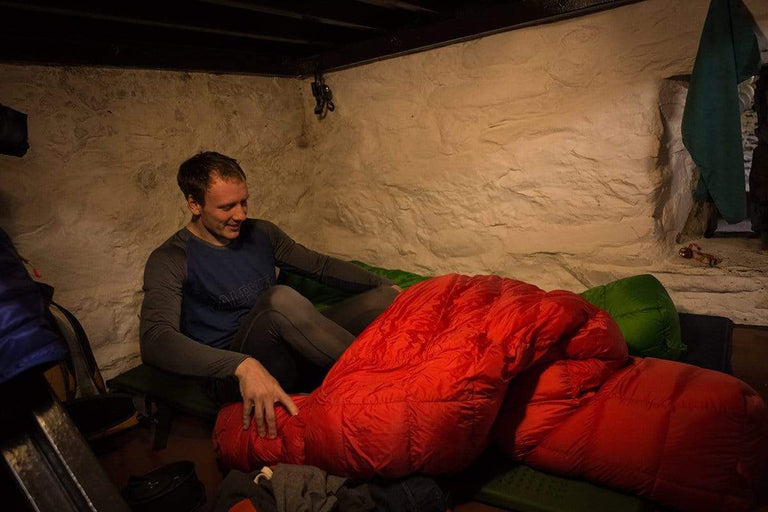 A man wearing merino wool base layers getting into his sleeping bag in a bothy - action - close