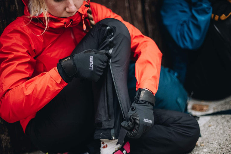 A woman sat on the floor doing up the zip on her waterproof trousers - action