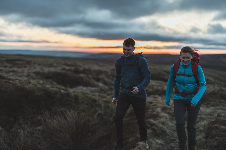 A man and a woman walking across moorland wearing wind resistant fleeces - action