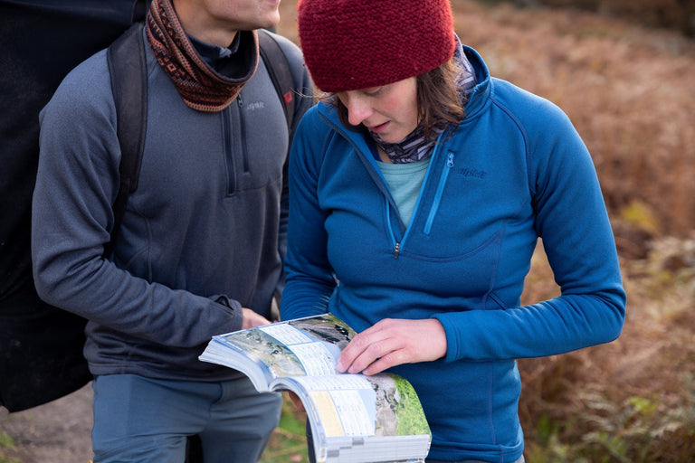 A man and a woman looking at a climbing guidebook wearing climbing fleeces - action - closed