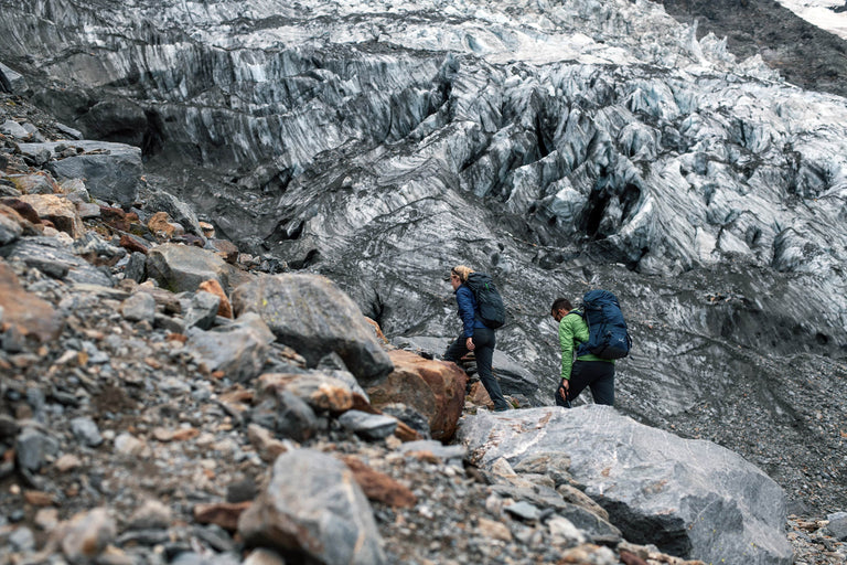 A man and a woman with backpacks on walking next to a glacier - action - closed