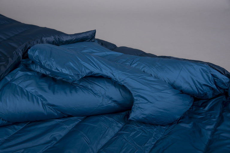 The hood end of a Pipedream 400 lightweight 3 season sleeping bag in blue with the zip open and laid on the floor on a grey background