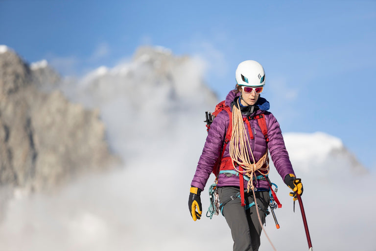 A woman walking across snow covered mountains in a purple down jacket