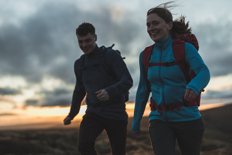 A man and a woman walking at sunset in the Peak District wearing a bright blue fleece jacket - action