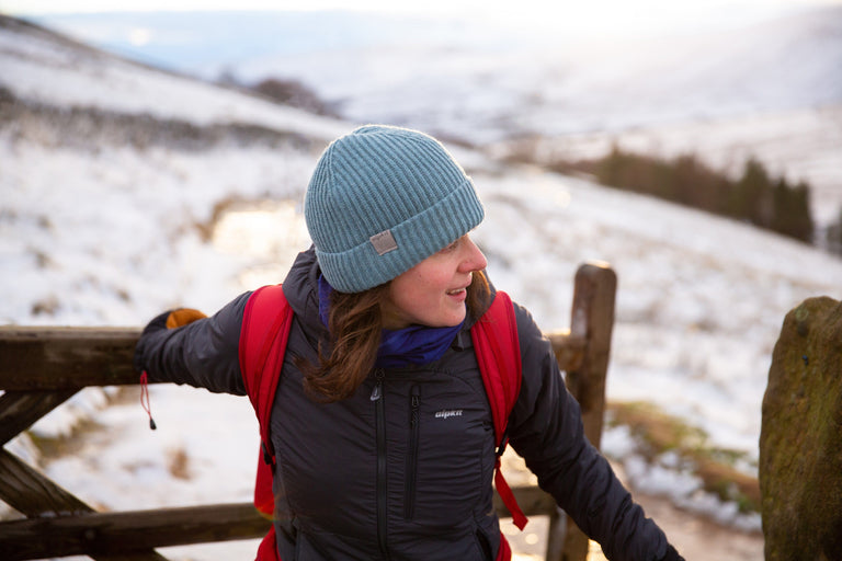 A woman walking through a gate in the snowy Peak District, wearing a dark grey insulated jacket - action - closed