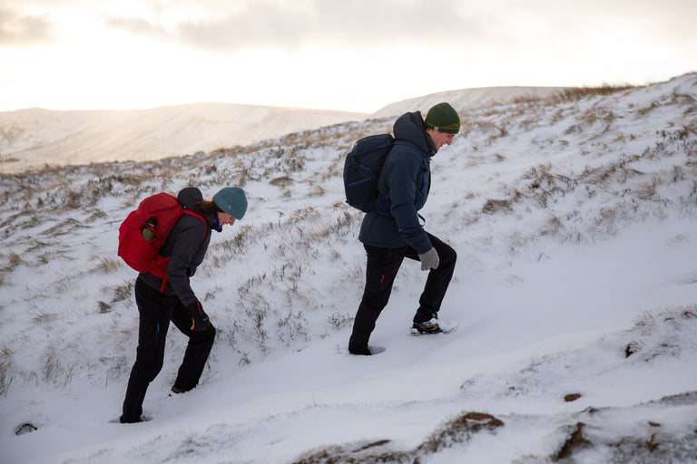 A man and a woman hiking up a steep snowy bank in the Peak District - action - closed