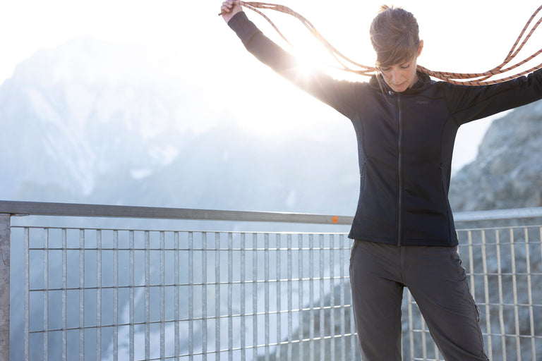 A woman coiling rope in the French Alps wearing a black hooded fleece jacket - action