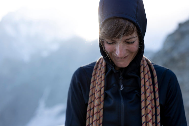A woman coiling rope in the French Alps wearing a black hooded fleece jacket - action