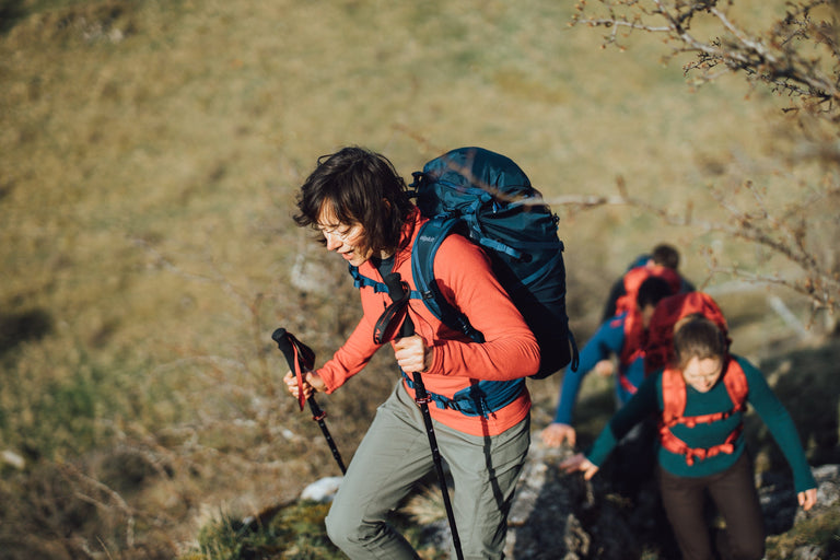 A woman hiking up a steep bank with trekking poles wearing a red fleece - action