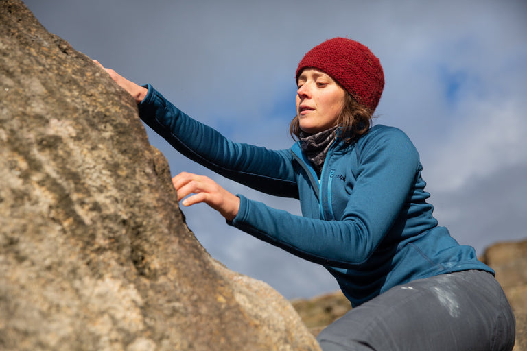 A woman bouldering in a stretchy blue fleece - action